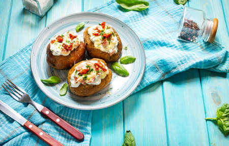 Baked stuffed potatoes with bacon, tomato and cheese on blue wooden background.