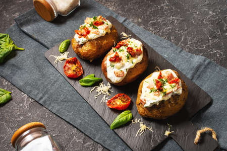 Baked stuffed potatoes with bacon, tomato and cheese on black stone background.の写真素材