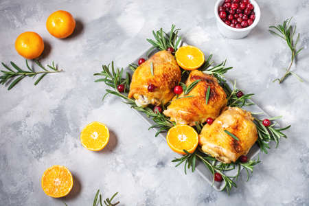 Christmas food. Chicken meat baked with cranberries, tangerines and rosemary on concrete backgroundの写真素材