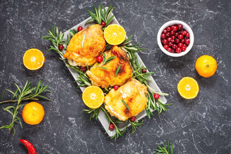 Christmas food. Chicken meat baked with cranberries, tangerines and rosemary on black stone backgroundの写真素材