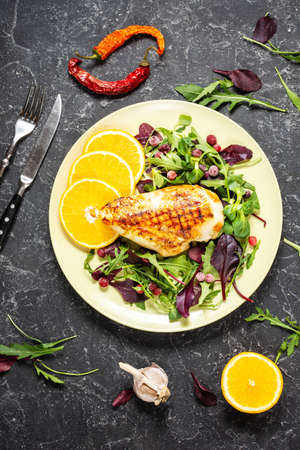 Grilled chicken breast and orange on green salad on dark stone background. Healthy eating conceptの写真素材