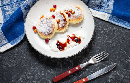 Cottage cheese pancakes on a dark stone background. Syrniki with sour cream. Homemade food. Top viewの写真素材