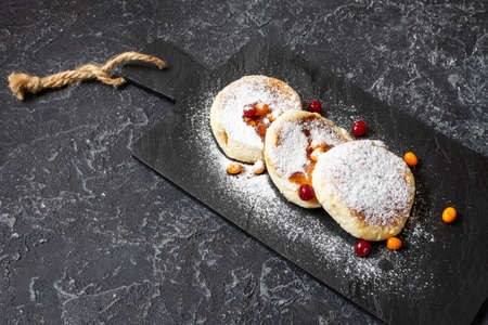 Cottage cheese pancakes on a dark stone background. Syrniki with sour cream. Homemade food.