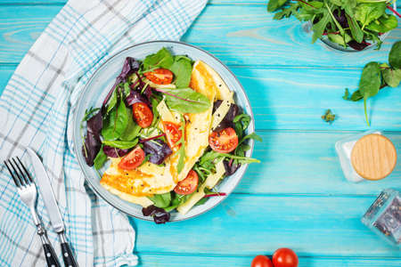 Herb omelette with cheese, cherry tomatoes and arugula on blue wooden background. Breakfastの写真素材