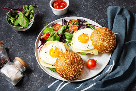 Breakfast two burgers with chicken, fried egg and cheese on a dark stone background