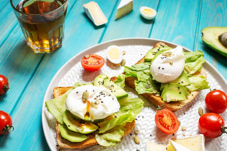 Healthy sandwich - poached eggs and avocado on toast with tomatoes on a blue wooden background.