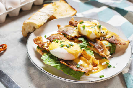 Sandwich with Eggs Benedict, bacon and salad on a concrete background.
