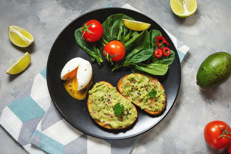 Healthy toast with avocado mexican sauce guacamole, boiled egg, cherry tomatoes and salad on concrete background. Top viewの写真素材
