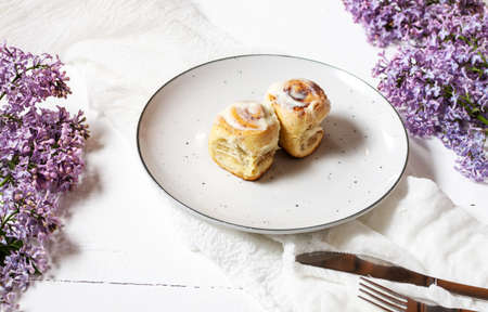 Cinnamon roll or cinnabon with white cream glaze on plate on white wooden background. Traditional homemade sweet bunsの写真素材
