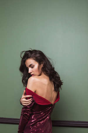 Pretty young woman in dress standing back against green wall.
