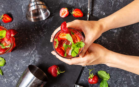 Female hands holds a glass of Strawberry mojito on black stone background. Topの写真素材