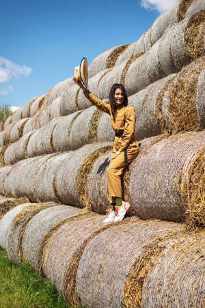 Young woman in overalls and hat at haystack. Female portrait in field in countryside.の写真素材