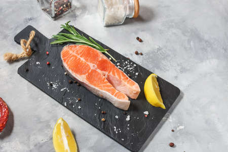 fresh raw salmon steak with salt, peppers, lemon, and rosemary on concrete background