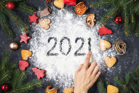 Happy New Year 2021 written on flour and Christmas Decorations Gingerbread cookies on dark stone background. New Year greeting cardの写真素材