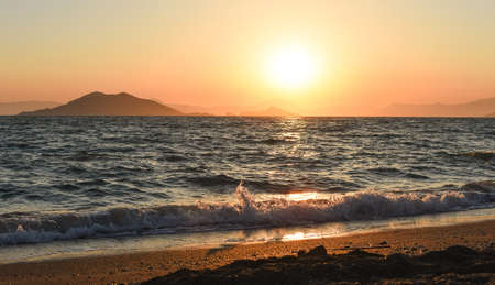 Amazing beach sunset with endless horizon and lonely figures in the distance, and incredible foamy waves. Volcanic hills in the background.の写真素材