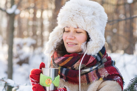 A young woman stands in a winter forest or park and drinking hot tea.の写真素材