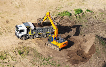 Industrial truck loader excavator moving earth and unloading into a dumper truck