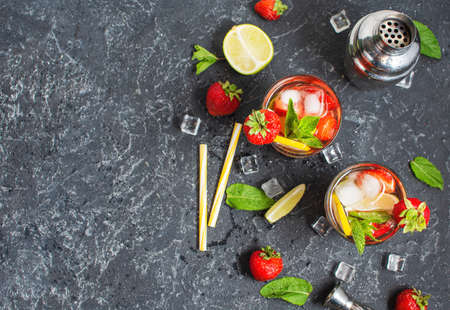 Summer refreshing mojito cocktail with strawberry, mint and lime with shaker for whipping drinks on a dark stone table. Top view and copyspaceの写真素材