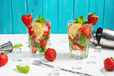 Summer refreshing mojito cocktail with strawberry, mint and lime with shaker for whipping drinks on white wooden tableの写真素材