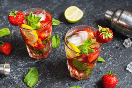 Summer refreshing mojito cocktail with strawberry, mint and lime with shaker for whipping drinks on dark stone tableの写真素材