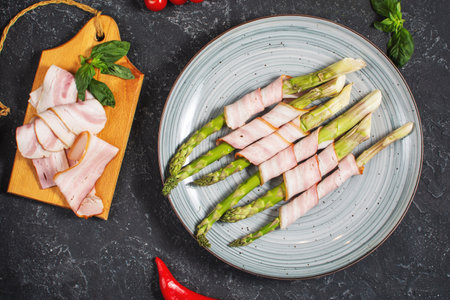 Fresh green asparagus wrapped in bacon on a black stone table. top viewの写真素材