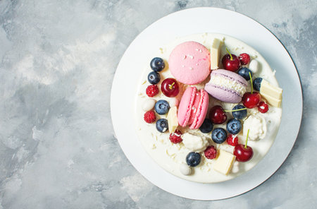 Tender white cake decorated with melted white chocolate, macaroons, meringues, berries and candies on concrete background. top viewの写真素材