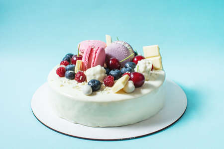 Tender white cake decorated with melted white chocolate, macaroons, meringues, berries and candies on blue background.の写真素材