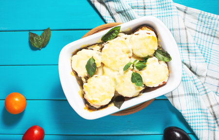 Eggplant baked with mozzarella cheese, tomatoes in baking dish on a blue wooden table. Vegetarian food recipe. top viewの写真素材