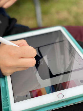 A girls hand drawing on an iPad or on a tablet. the drawing is a smartphone.