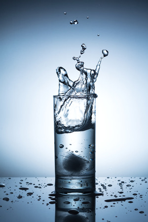 Ice cubes splashing into glass of waterの写真素材