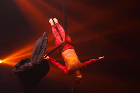 Brazilian strong sexy man do performance on aerial silks in red lights. Sport training gym and lifestyle concept. Black background. Gymnast upside down on aerial silkの写真素材