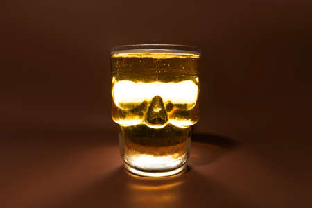 Refreshing and cold glass of beer shaped like skull isolated over brown background in a studio shot. Hallowen concept.の写真素材