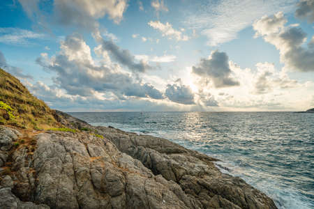 Rocky ocean coast in front of beautiful sunset lights, waves hits rocks in cloudy weatherの写真素材