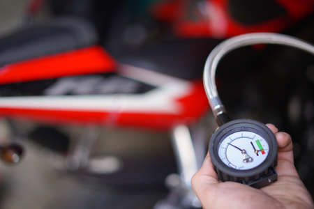 Man checking manually air pressure of motorcycle wheel before traveling. The air pressure is...