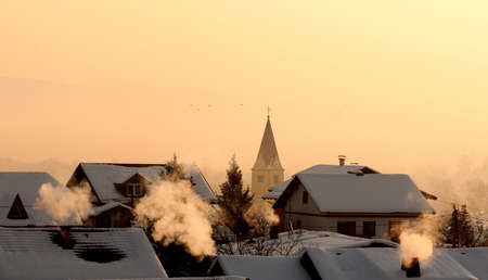 Very cold morning over houses and church roofs, smoke rises from chimney.の写真素材