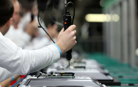 Man working on assembly line assembling TV sets using electric screwdriverの写真素材
