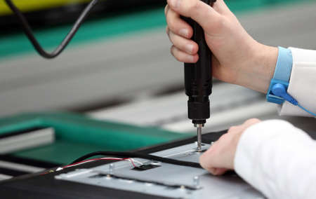 Man working on assembly line assembling TV sets using electric screwdriver
