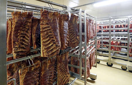 Piaces of meat, pork ribs hanging in big fridgeの写真素材