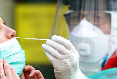 Medical staff member with mask, rubber gloves and protective equipment performs Coronavirus nasal swabs to patient at drive-through testing point in an effort to curb the spread of COVID-19 (novel coronavirus)の写真素材