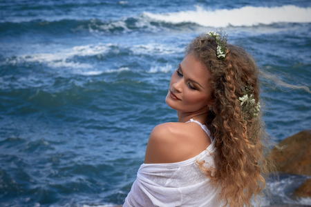 portrait of pretty sensual curly girl with flowers in her head, white dress, sea view, nature beauty photography, summer travelingの写真素材