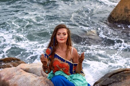 ethnic fashion outdoor photo of beautiful sexy girl in bright clothes yoga posing on summer sea beach, sensual relaxed mood , boho style wearの写真素材