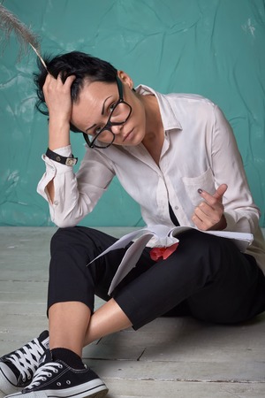 Young business woman in glasses thinking, work with documents, sitting on the floor in studio with blue walls, creative work spaceの写真素材