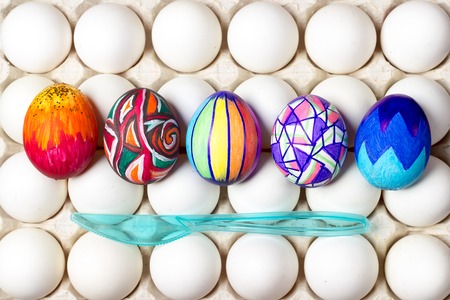 five multicolored painted easter eggs lying on white tray, different patterns, blue knife, holiday celebration food photographyの写真素材