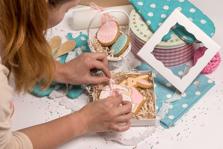 girl cooker puts easter rabbit honey-cake in special box, nice details on table in blue colors, holiday family present preparations, kitchen designの写真素材