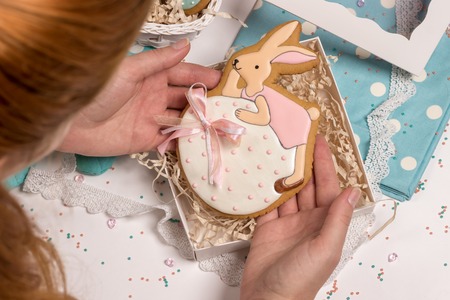 girl cooker puts easter rabbit honey-cake in special box, sweet cake in form of egg, nice details on table in blue colors, holiday family present preparations, kitchen designの写真素材