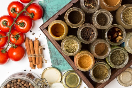 Close photo of spices and herbs, small glass jars.  Food, cuisine ingredients: carry chilly turmeric, blue painted wooden board. Cherry tomatoes branch. Food, cuisine ingredients photography.の写真素材