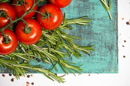 branch of fresh cherry ripe tomatoes, fresh rosemary on blue wooden board, food photographyの写真素材