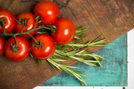 branch of fresh cherry ripe tomatoes, fresh rosemary on blue wooden board, food photographyの写真素材