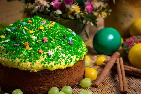 Easter celebrating family dinner, multicolored eggs, flowers, sweet sprinkled cakes, cupcakes, fruit herbal tea,  sweets on wooden table, food holiday photoの写真素材