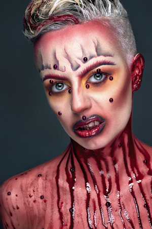 Creative makeup, new crazy conceptual idea for Halloween. black red bold body art painting. Crazy new fashion makeup, wet bloody body, streaks on woman face. shiny lipstick gloss lips conceptual professional photoの写真素材